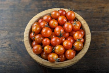 Kahverengi ahşap zemin üzerinde ahşap bir tabakta kiraz domatesleri. Yukarıdan görünüm