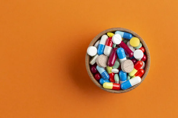 Assorted pharmaceutical medicine pills, tablets and capsules on wooden bowl. Pharmaceutical industry concept. Antibiotic drug resistance.