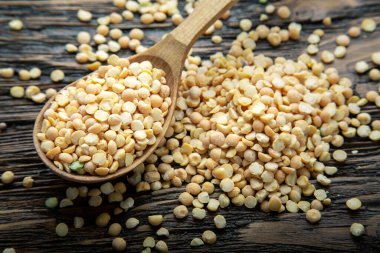 Kahverengi ahşap bir arka planda kaşıkta kuru bezelyeler. Besleyici sou için fasulye