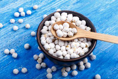 Kil tabakta kuru nohut ve mavi ahşap arka planda bir kaşık. Tabağın yanındaki nohutlar dağılmış.