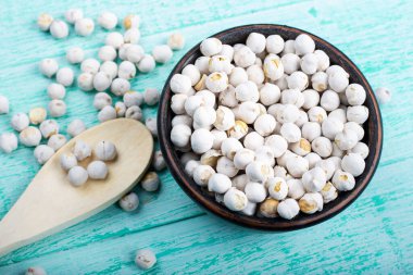 Çamurdan bir tabakta ahşap bir zeminde pişmemiş kuru beyaz nohutlar. Yakınlarda bir kaşık yatar.