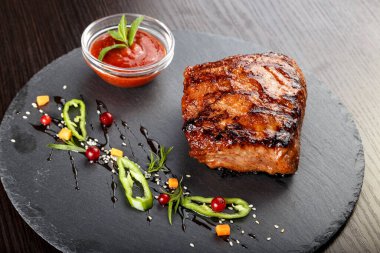 Biftek tahtada. Ketçaplı bir sos teknesinin yanında duruyordu. Tahtada acı biber, doğranmış havuç, kırmızı frenk üzümü ve susam var..