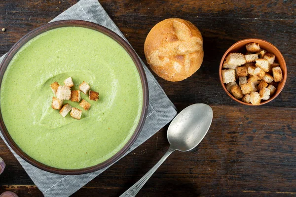 stock image green broccoli cream soup in a plate on the table. next to them are fresh buns. the soup is decorated with cracker