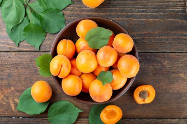 Ahşap bir zeminde, bir masada, kil bir tabakta olgun kayısılar. Kayısıların yanında yeşil izin.