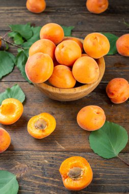 Ahşap arka planda, masanın üzerinde, ahşap bir tabakta olgun kayısılar. Kayısıların yanında yeşil izin.