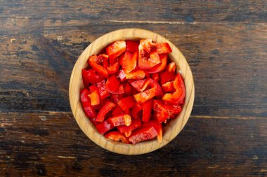 Kahverengi ahşap arka planda bir tabakta doğranmış kırmızı dolma biber