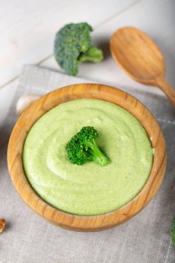 Masadaki ahşap tabakta yeşil brokoli kremalı sebze çorbası. Brokoli ile süslenmiş çorba.