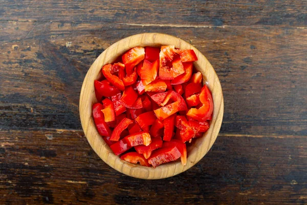 Kahverengi ahşap arka planda bir tabakta doğranmış kırmızı dolma biber