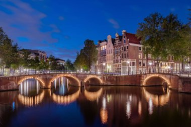 Kanallardaki aydınlatılmış köprülerin panoraması geceleri. Amsterdam şehri, Hollanda Alacakaranlıkta
