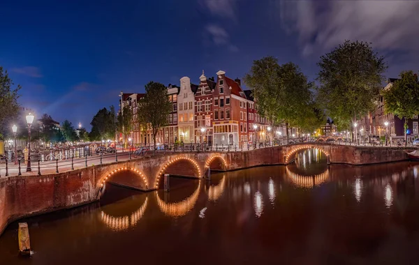 Kanallardaki aydınlatılmış köprülerin panoraması geceleri. Amsterdam şehri, Hollanda Alacakaranlıkta — Stok fotoğraf