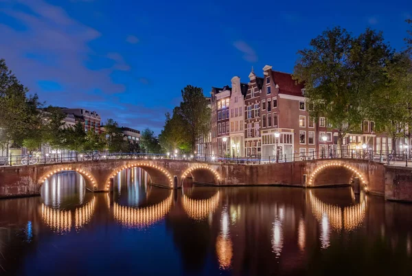 Panorama osvětlených mostů v noci na kanálech. Město Amsterdam, Nizozemsko za soumraku — Stock fotografie