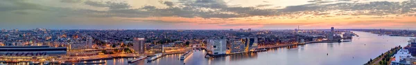 Panorama degli edifici illuminati, della Stazione Centrale e dei moli al tramonto. Paesaggio urbano di Amsterdam, Paesi Bassi al crepuscolo — Foto Stock