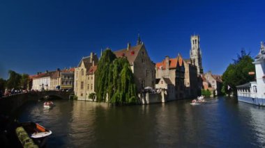 Güneşli bir günde arka planda çan kulesiyle Bruges kanallarının manzarası.