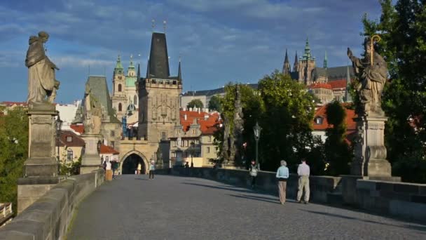 A turisták ellátogatnak a Károly hídra egy napsütéses napon. Prágai vár és Szent Vitus katedrális a háttérben. — Stock videók