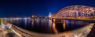 Aydınlatılmış Hohenzollern Köprüsü 'nün Ren Nehri üzerindeki gece panoraması. Köln, Almanya 'nın güzel şehirleri. Arkasında katedral ve büyük St. Martin Kilisesi var.