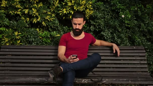年轻而有自信的胡子男人在公园用他的电话 — 图库视频影像