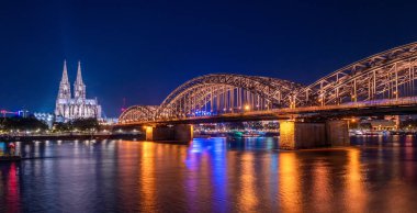 Aydınlatılmış Hohenzollern Köprüsü 'nün Ren Nehri üzerindeki gece panoraması. Köln, Almanya 'nın güzel şehirleri. Arkasında katedral ve büyük St. Martin Kilisesi var.