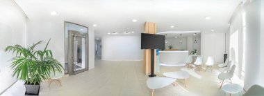 Panorama of a bright reception and waiting room in a clinic with desk, modern chairs and plants. Indoor mockup with screen with copy space. clipart