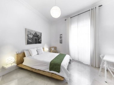 Büyük boy yatağı, yorganı, komodinleri, lambaları, fotoğrafçılığı olan temiz bir yatak odası. Minimalist beyaz stil iç mekan