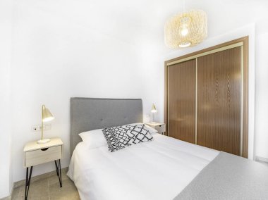 Doğal kumaş yastıklı keçeli yatak odası, rattan lamba, ahşap komodin ve büyük, ahşap bir gardırop. İskandinav tarzında tatil yeri dairesi.