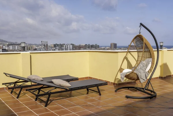 Hanging chair and sun beds in a sunny terrace of a relaxing summer holiday destination with sea view.