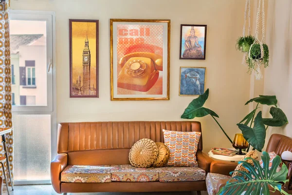 Zabytkowe dekoracje wnętrz z sofą retro, stare plakaty, wieszaki na rośliny makramy, poduszki do przedruku. — Zdjęcie stockowe