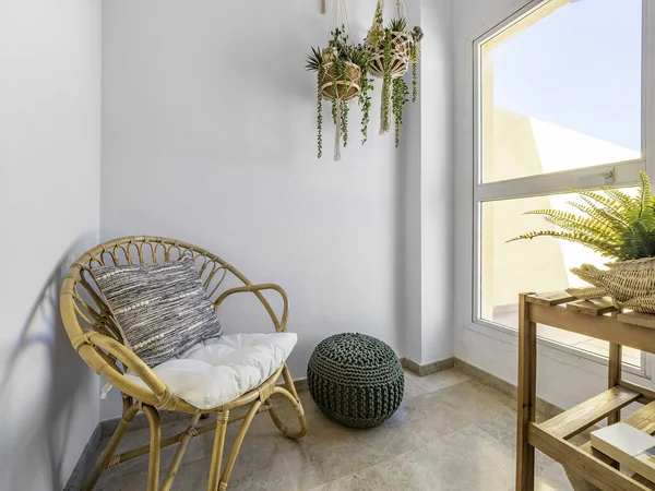 İçinde minderli rattan sandalye, makrome asılı bitkiler ve büyük pencereli bir oturma odasında fiber puf olan bir oda. Dinlenme odasında gevşe. Hygge dekorasyon konsepti.