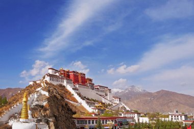 Yeşil bitki örtüsüyle çevrili Lhasa, Tibet 'teki Potala Sarayı' nın yan manzarası beyaz bulutlarla kaplı mavi bir yaz gökyüzüne karşı..