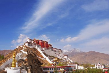 Lateral view of the Potala Palace in Lhasa, Tibet, surrounded by green vegetation, against a blue summer sky covered by white clouds. clipart