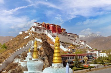 Yeşil bitki örtüsüyle çevrili Lhasa, Tibet 'teki Potala Sarayı' nın yan manzarası beyaz bulutlarla kaplı mavi bir yaz gökyüzüne karşı..