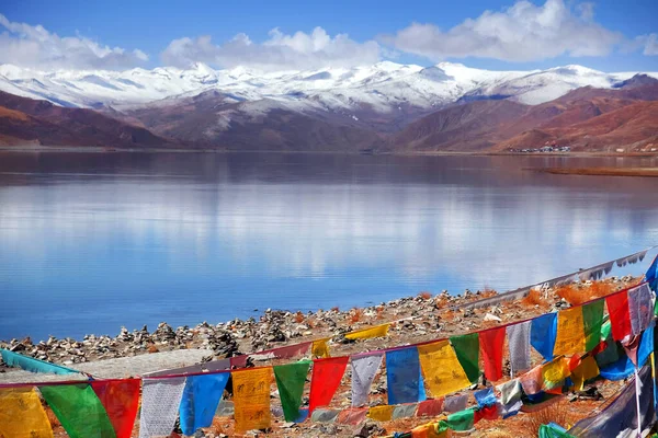 Tibeti imádkozó zászlók előtt a Yamdrok-tó, tükrözve a barna színek a Mt. Naiqinkangsang a kék tiszta égbolton. — Stock Fotó