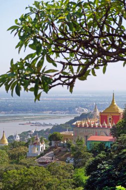 Mandalay, Myanmar 'da, yeşil bitki örtüsüyle çevrili, Irrawaddy Nehri' nin kenarındaki Budist tapınaklarının dikey görüntüsü..