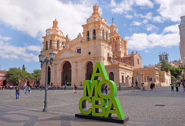 Lateral view of Cathedral of Cordoba, Argentina and a green text sculpture, against a blue sky covered by white clouds. — ストック写真