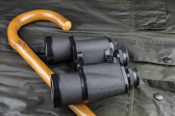 Bastón de caminar y prismáticos en un abrigo al aire libre — Foto de Stock
