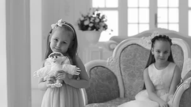 Een meisje met een speelgoed-engel in haar handen. Meisjes in slimme jurken thuis op eerste kerstdag. — Stockvideo