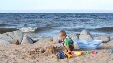 Küçük sarışın çocuk kumsalda oynarken. Çocuk kum kum ve oyuncaklar ile oynama okyanus üzerinde yürür.
