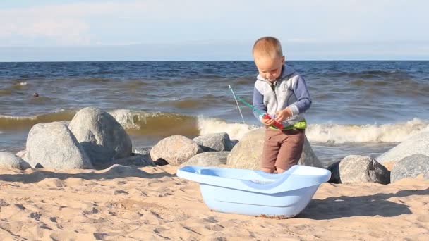 少年は海の海岸に砂と梨で遊んでいます 金髪の子供は夏にビーチで遊んで — ストック動画