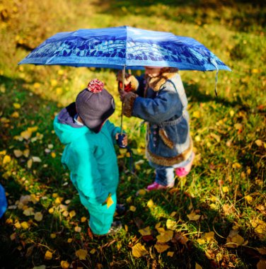Küçük kız ve erkek yağmurda oynarken şemsiye ile. Çocuklar tarafından Yağmurlu hava sonbaharda açık oynar. Sonbahar eğlenceli çocuklar için. Yürümeye başlayan çocuk yağmurluk ve çizmeler yürümek içinde belgili tanımlık Bahçe.