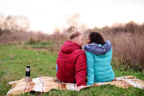 Young couple sitting on the plaid and drink coffee from a thermo — Stock Photo, Image