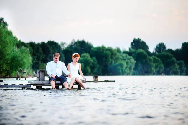 Casal de casamento jovem bonito, noiva e noivo posando no fundo do lago. O noivo e a noiva no cais — Fotografia de Stock