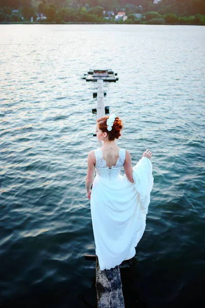 Noiva em pé na doca perto da água em um vestido branco — Fotografia de Stock