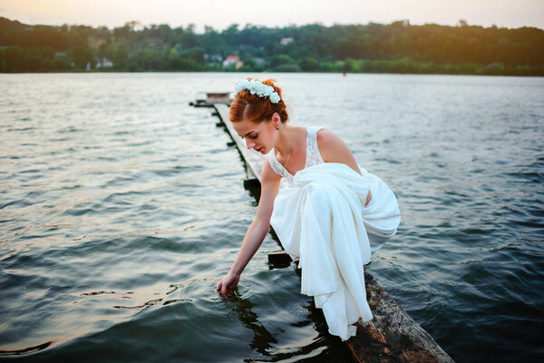 Bride standing on the dock near the water in a white dress.