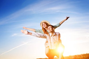 Genç adam neşeli kız arkadaş gibi gökyüzü arka plan üzerinde uçak piggybacking