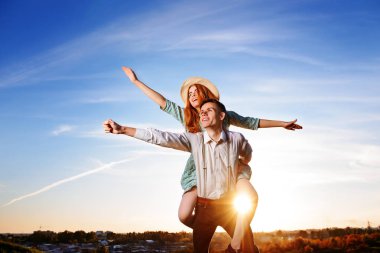 Genç adam neşeli kız arkadaş gibi gökyüzü arka plan üzerinde uçak piggybacking