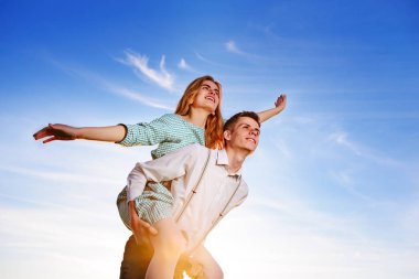 Genç adam neşeli kız arkadaş gibi gökyüzü arka plan üzerinde uçak piggybacking