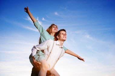 Genç adam neşeli kız arkadaş gibi gökyüzü arka plan üzerinde uçak piggybacking