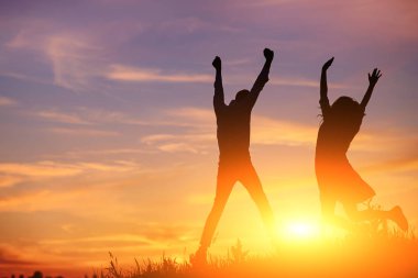 Genç bir adam onun kız arkadaşı ile atlama üzerinde arka plan günbatımı siluet