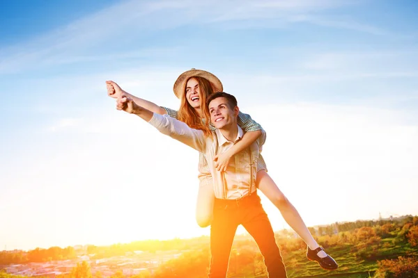 Junger Mann huckepack seine glückliche Freundin mit erhobener Hand. fröhliche Verliebte träumen — Stockfoto