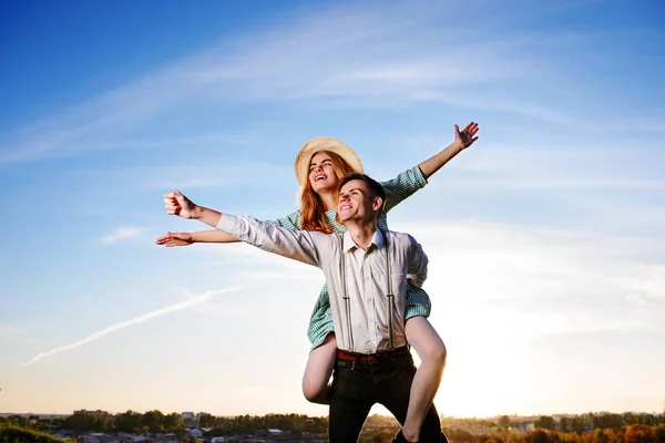Jonge kerel meeliften vrolijke vriendin als vliegtuig op de achtergrond van de hemel — Stockfoto