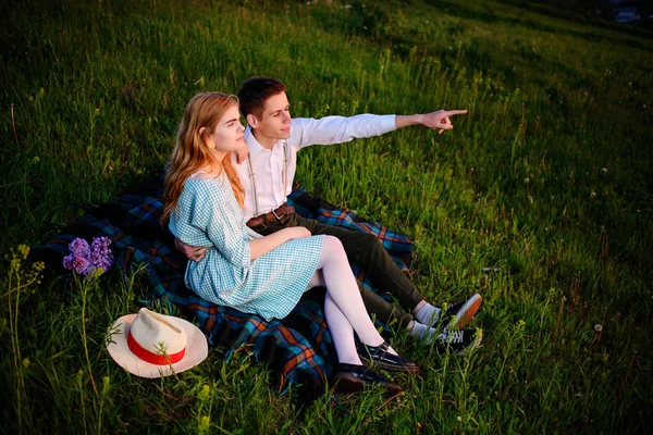 Νεαρό ζευγάρι κάθεται στο plaid για το πάρκο και να εξετάσουμε το ηλιοβασίλεμα, ο άνθρωπος είναι στραμμένο στον ορίζοντα — Φωτογραφία Αρχείου